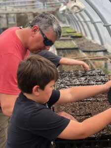 Father and Son planting pumpkin seeds in the greenhouse at Dirt farm Brewing. Father's Day celebration