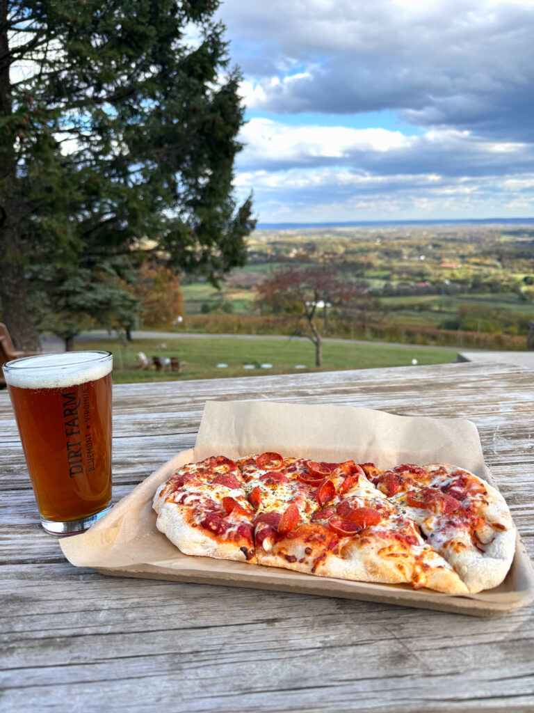 beer and pizza set out on the patio with the view from dirt farm brewing in the background as guests celebrate happy hour
